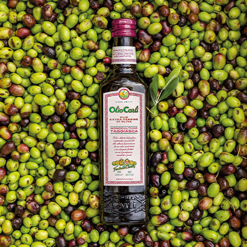 Bottiglia di Olio Carli Extra Vergine di Oliva Monocultivar Taggiasca adagiata su un letto di olive.