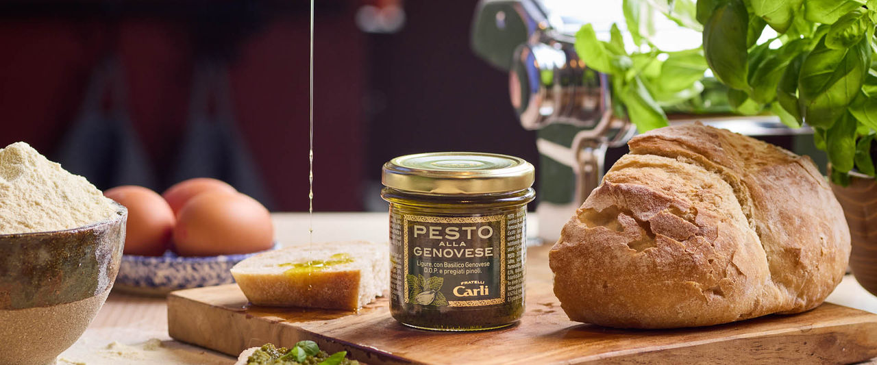 Vasetto di Pesto Fratelli Carli anbientato su tagliere, pane, fetta di pane e filo d'Olio che la condisce