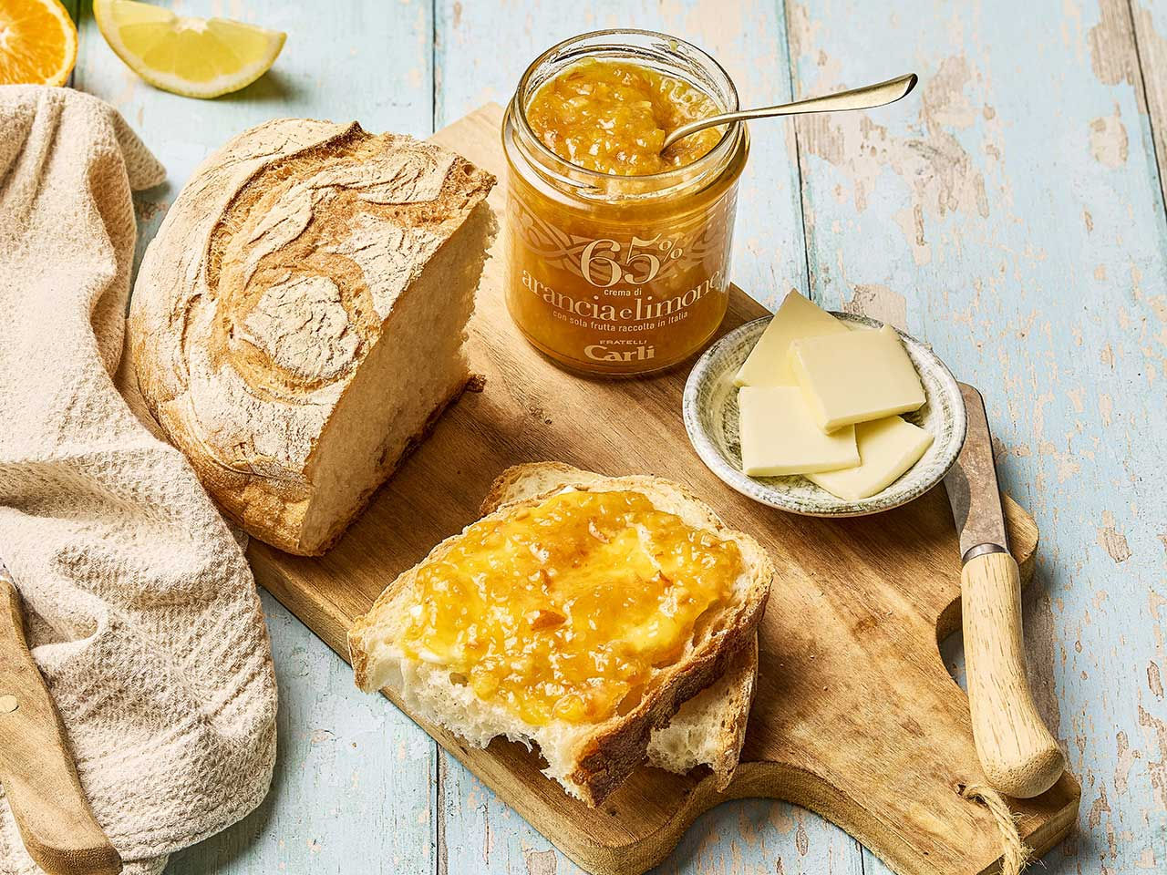 Una fetta di pane spalmata di Crema di arancio e limone Fratelli Carli accanto al vasetto che contiene la Crema